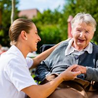 Nurse holding hands with senior woman sitting in wheelchair in garden of retirement home